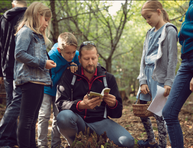 On a hiking trial, a father and his children look at a guidebook that references rabies information